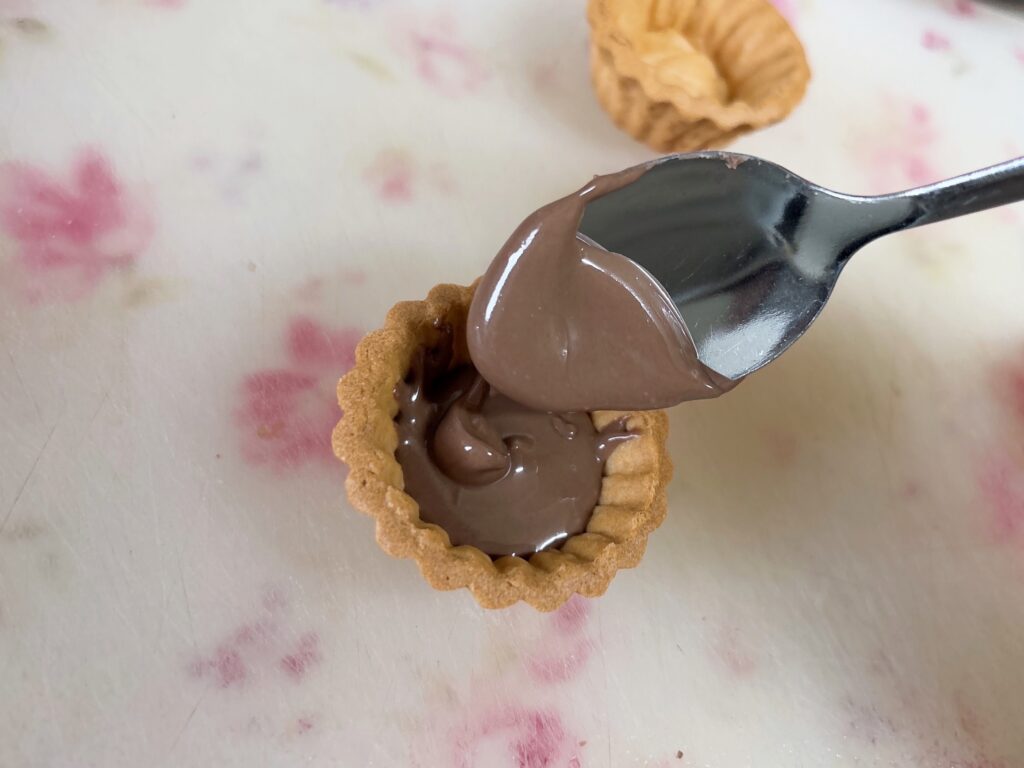 タルトカップに溶かしたチョコをスプーンで入れているところ